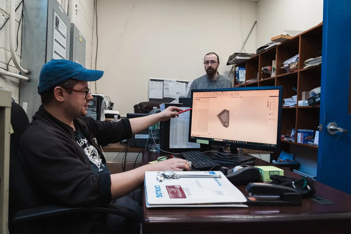 Engineer at a workstation pointing at a formed part in a 3D model