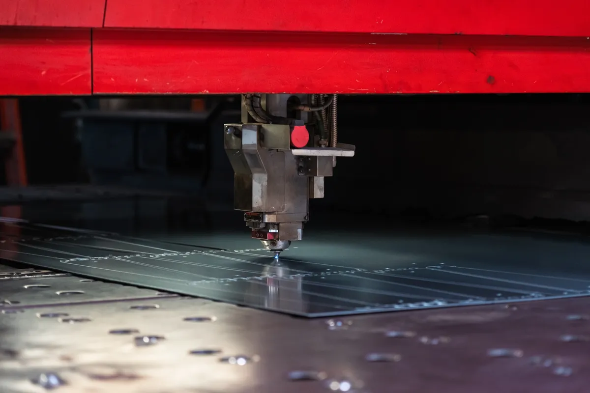 Laser cutting head mid-cut on the bed with a red glow at the nozzle