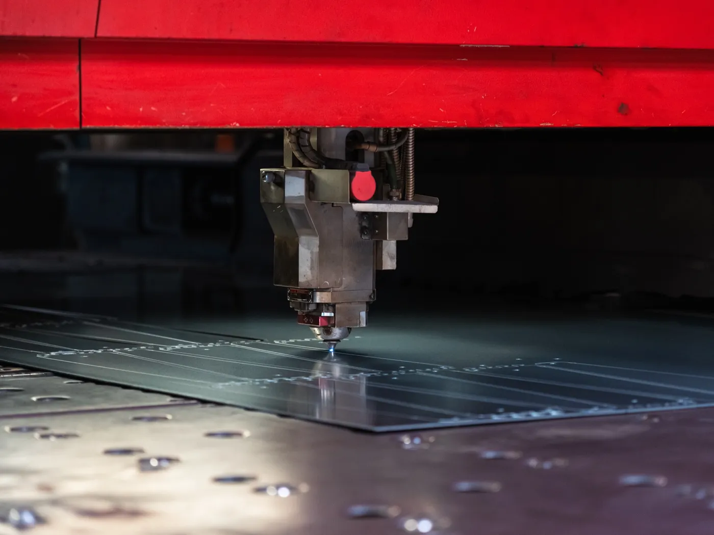 Laser cutting head mid-cut on the bed with a red glow at the nozzle