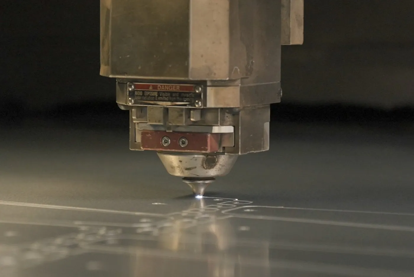 Laser nozzle tracing a part outline in a sheet of steel, sparks at the kerf