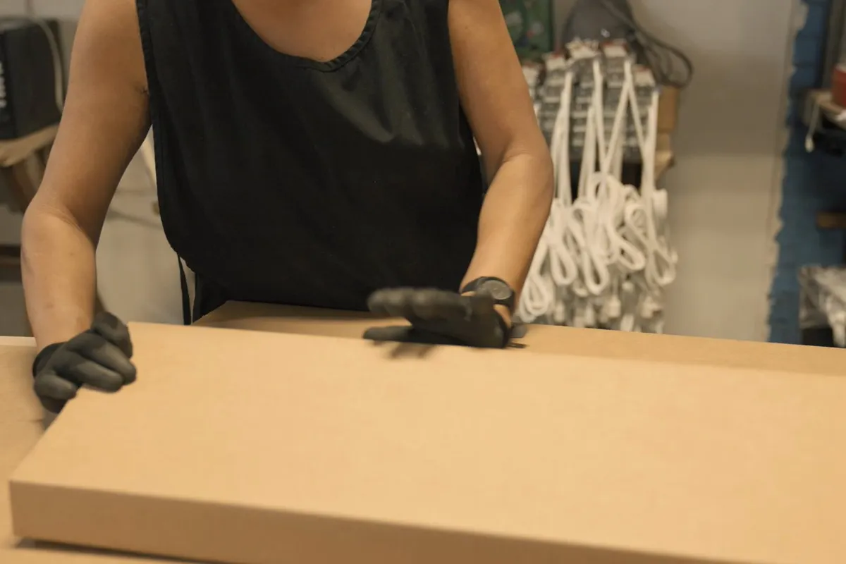 Operator folding a carton at the packing bench with wire forms behind