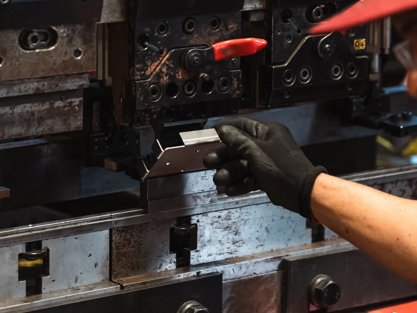 Gloved hands feeding a metal blank into a press brake