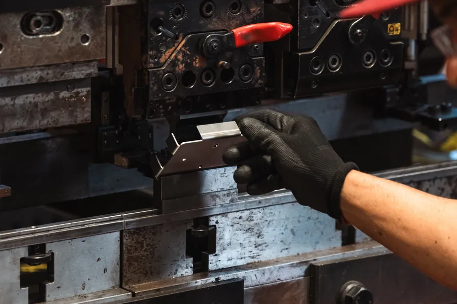 Gloved hands feeding a metal blank into a press brake