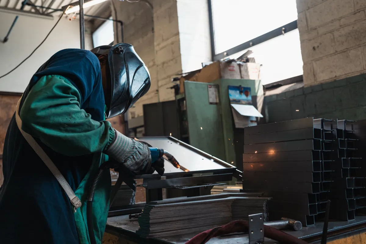 Welder in a green jacket and hood with sparks flying